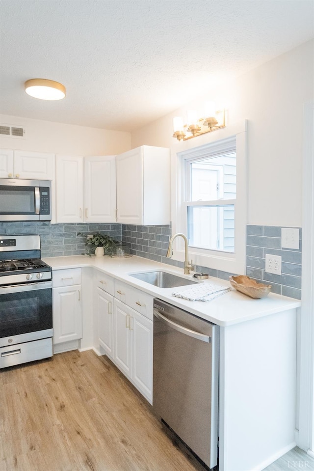 3501 Fort Ave Unit 27, Lynchburg, VA 24501 - kitchen with stainless steel appliances, a sink, light wood-style floors, decorative backsplash, and white cabinetry