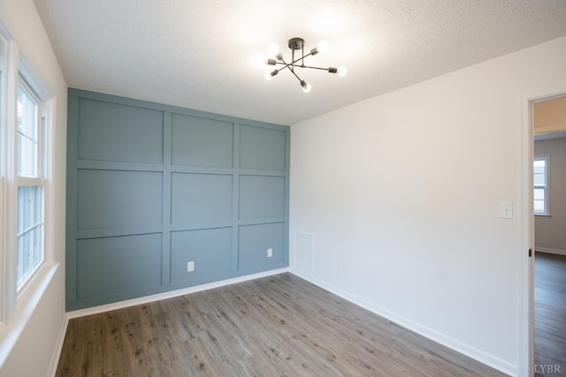 3501 Fort Ave Unit 27, Lynchburg, VA 24501 - spare room featuring a decorative wall, a chandelier, light wood finished floors, baseboards, and a textured ceiling