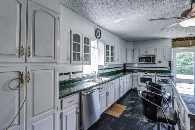 kitchen with stainless steel appliances, dark countertops, glass insert cabinets, a textured ceiling, and a ceiling fan