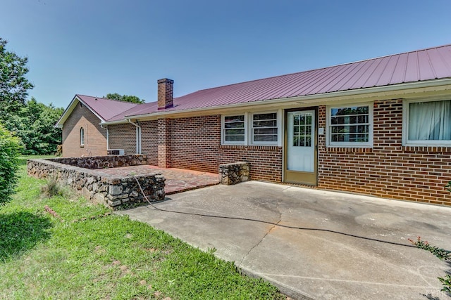 rear view of house with a patio, a chimney, a metal roof, and brick siding