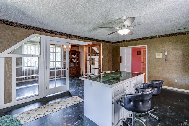 kitchen featuring ceiling fan, a textured ceiling, wallpapered walls, white cabinetry, and tile countertops