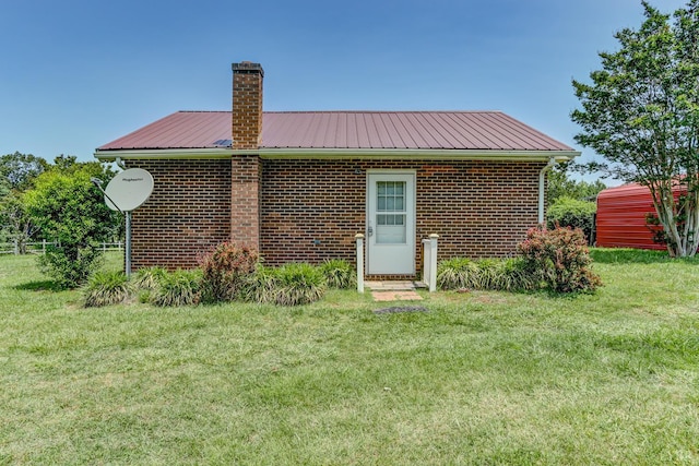 back of house with a chimney, a yard, a metal roof, and brick siding