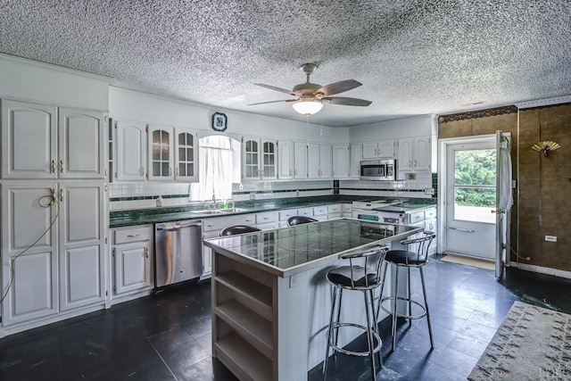 kitchen with appliances with stainless steel finishes, open shelves, a breakfast bar area, glass insert cabinets, and a kitchen island