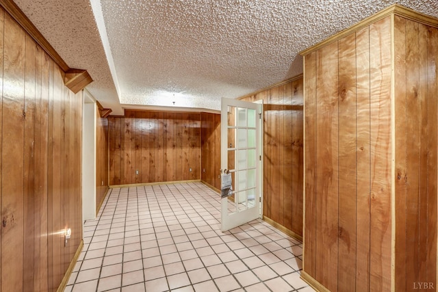 hallway with wooden walls, light tile patterned flooring, a textured ceiling, and crown molding
