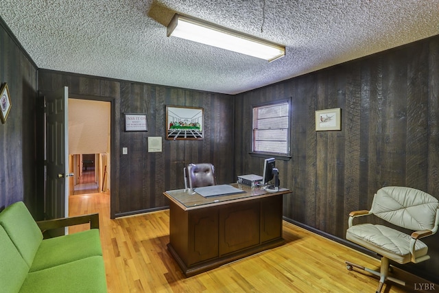 home office with a textured ceiling, light wood-style floors, and wooden walls