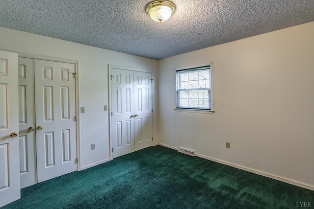 unfurnished bedroom with multiple closets, dark colored carpet, and a textured ceiling