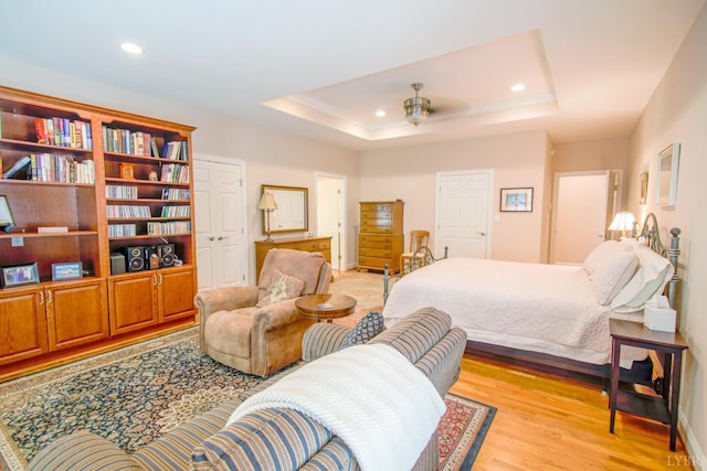 bedroom with light wood finished floors, recessed lighting, and a raised ceiling