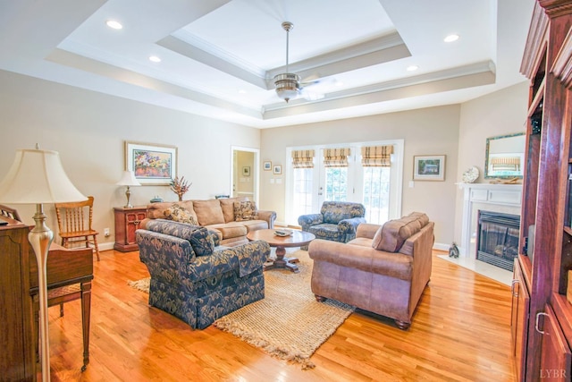 living room featuring a tray ceiling, light wood-type flooring, a fireplace with flush hearth, ornamental molding, and recessed lighting