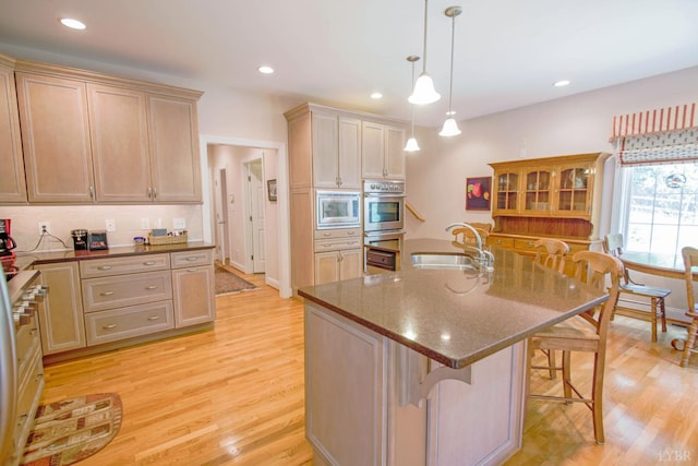 kitchen featuring a breakfast bar, light wood finished floors, appliances with stainless steel finishes, dark stone countertops, and hanging light fixtures