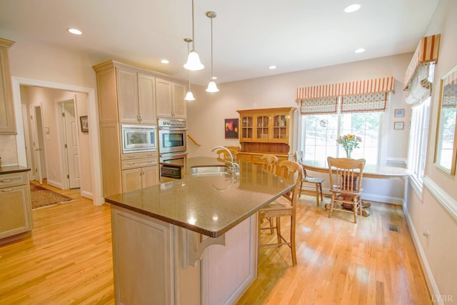 kitchen with appliances with stainless steel finishes, light wood-style flooring, a kitchen breakfast bar, pendant lighting, and recessed lighting