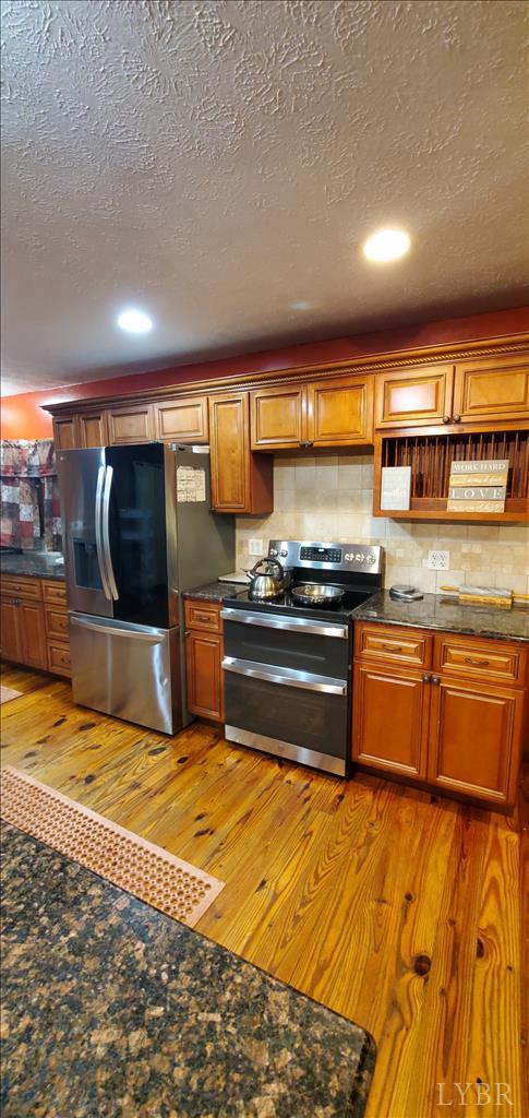 2995 Bear Creek Rd, Rustburg, VA 24588 - kitchen with appliances with stainless steel finishes, light wood-style flooring, decorative backsplash, a textured ceiling, and brown cabinets