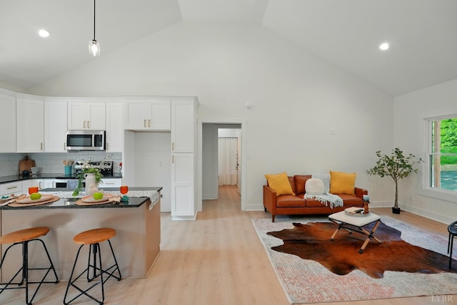 201 Thomas Rd, Lynchburg, VA 24501 - kitchen featuring appliances with stainless steel finishes, dark countertops, high vaulted ceiling, white cabinetry, and a kitchen bar