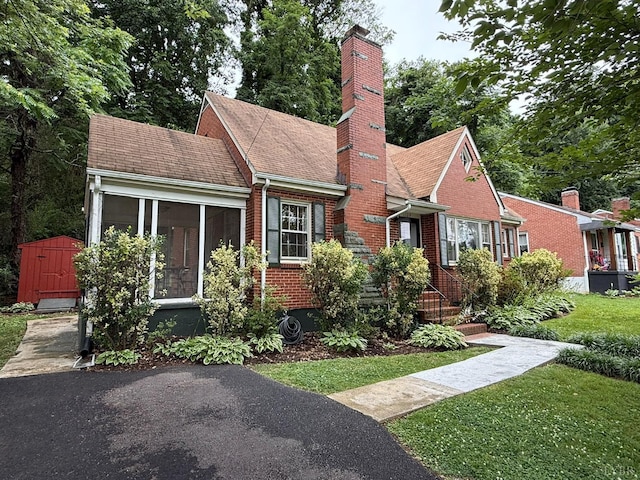 1309 Cherokee Ave, Lynchburg, VA 24502 - view of front of home with a sunroom, a chimney, brick siding, a storage unit, and a front lawn