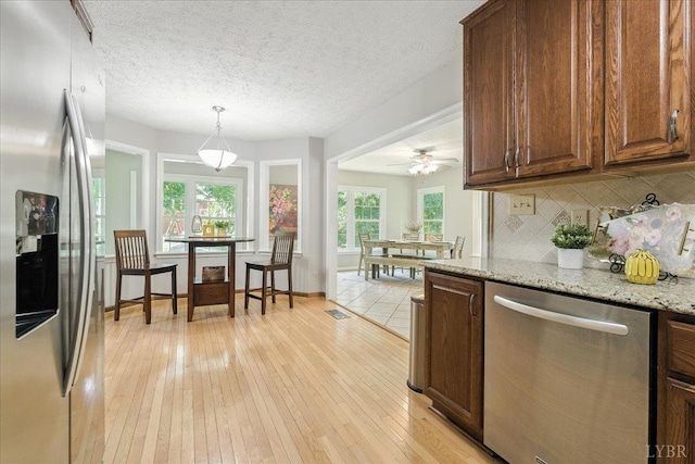 702 Kings Rd, Lynchburg, VA 24502 - kitchen featuring appliances with stainless steel finishes, decorative backsplash, light wood finished floors, light stone countertops, and hanging light fixtures