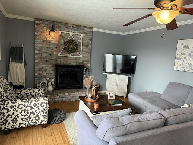 living room featuring a brick fireplace, a textured ceiling, ornamental molding, ceiling fan, and hardwood / wood-style floors