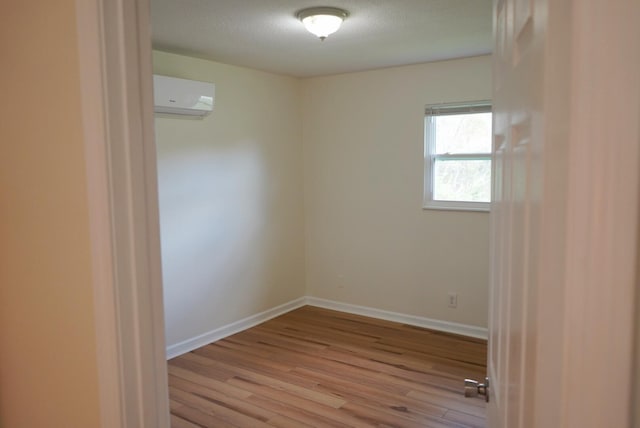 unfurnished room with light wood-type flooring, a textured ceiling, and a wall unit AC