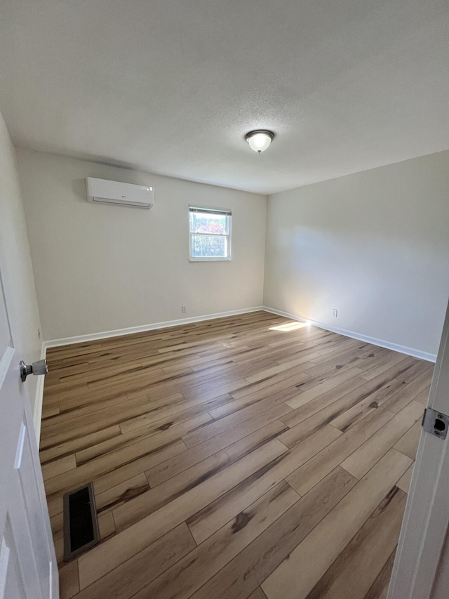 unfurnished room with a textured ceiling, light hardwood / wood-style flooring, and a wall unit AC