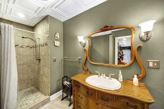 full bathroom with tile patterned floors, tiled shower, vanity, baseboards, and a textured wall