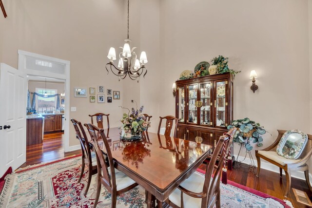dining space with an inviting chandelier, baseboards, a high ceiling, and wood finished floors