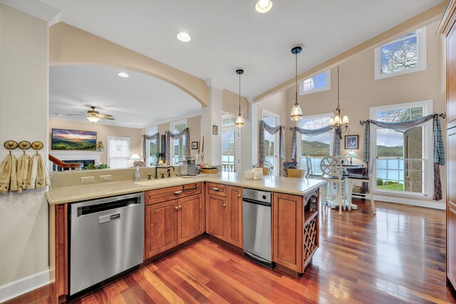 kitchen featuring light countertops, dishwasher, brown cabinets, arched walkways, and ceiling fan with notable chandelier