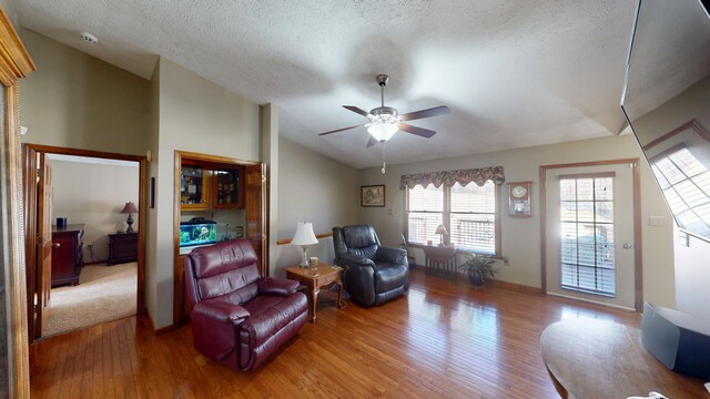 living room with a textured ceiling, ceiling fan, hardwood / wood-style floors, and vaulted ceiling