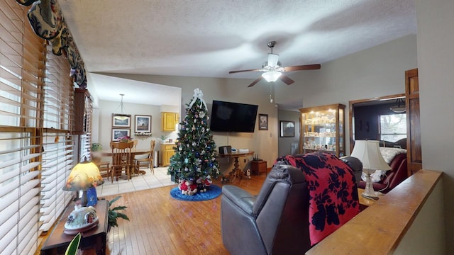 living room with a textured ceiling, ceiling fan, lofted ceiling, and light wood-type flooring