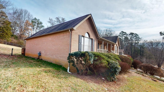 view of property exterior with brick siding, a lawn, and fence