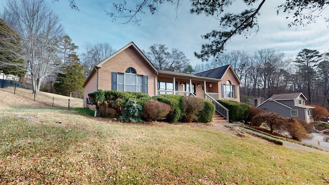 ranch-style house featuring covered porch, brick siding, a front yard, and fence