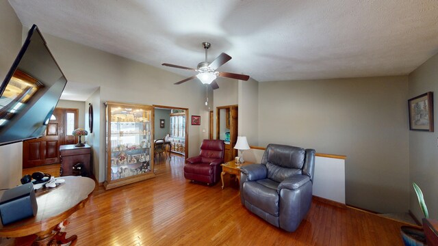 living room featuring a textured ceiling, light hardwood / wood-style floors, ceiling fan, and lofted ceiling