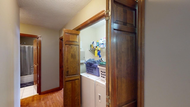 clothes washing area with washer and dryer, a textured ceiling, and light wood-type flooring