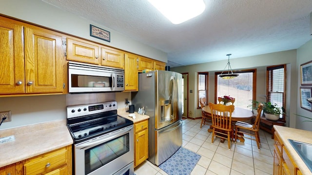 kitchen featuring sink, stainless steel appliances, decorative light fixtures, a textured ceiling, and light tile patterned flooring