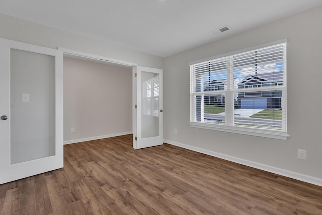 unfurnished room featuring french doors, visible vents, baseboards, and wood finished floors