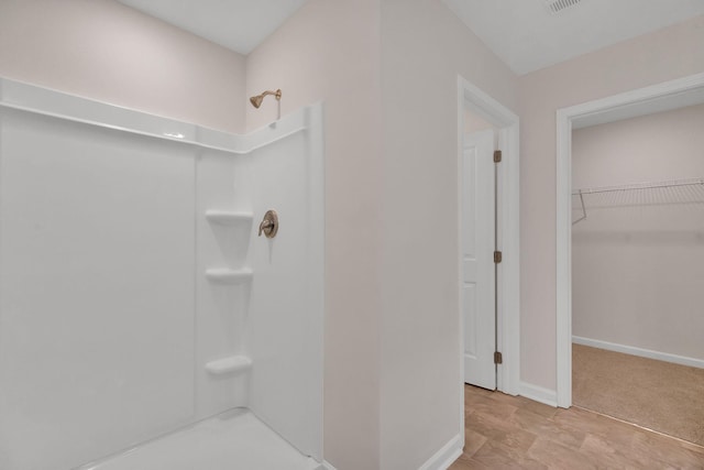 bathroom with a shower, a walk in closet, visible vents, and baseboards