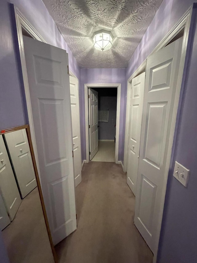 hallway featuring light carpet, baseboards, and a textured ceiling