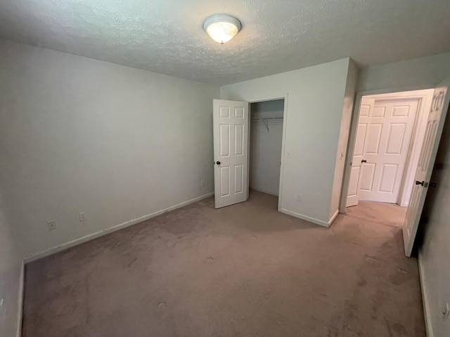 unfurnished bedroom with light colored carpet, a textured ceiling, baseboards, and a closet