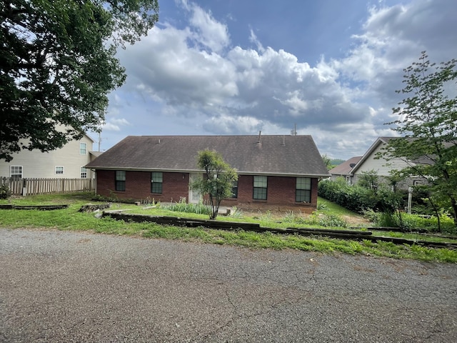 view of front of home with brick siding, fence, and roof with shingles
