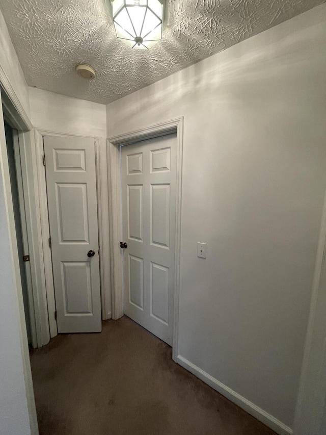 hallway featuring carpet flooring, a textured ceiling, and baseboards