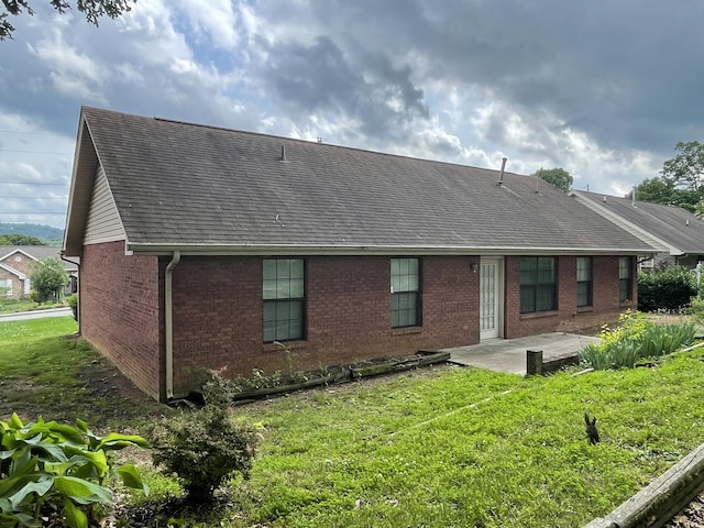rear view of house with brick siding, a patio, a lawn, and roof with shingles