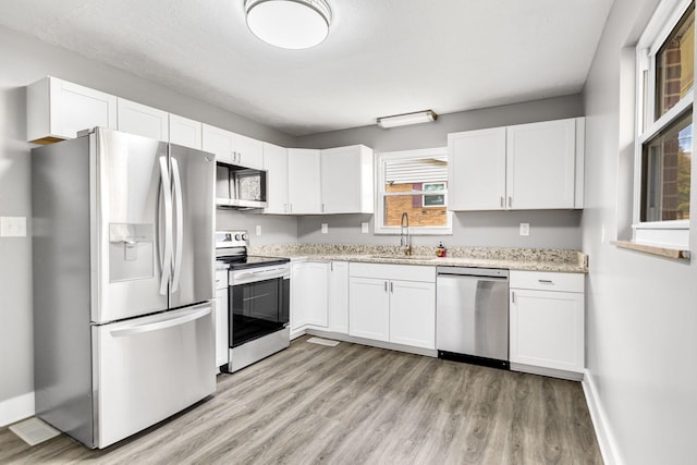 kitchen with sink, white cabinetry, light stone counters, light hardwood / wood-style flooring, and appliances with stainless steel finishes