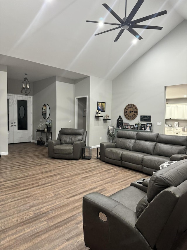 living room with wood finished floors, ceiling fan with notable chandelier, baseboards, and high vaulted ceiling