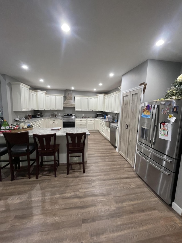 kitchen featuring dark wood-type flooring, a breakfast bar, white cabinetry, appliances with stainless steel finishes, and custom range hood