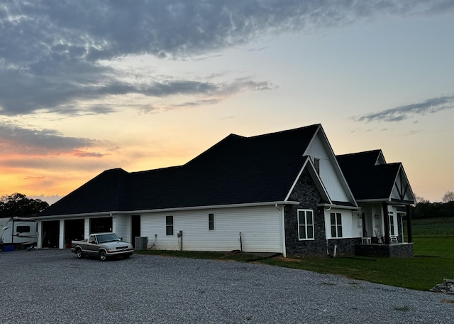 view of front facade featuring cooling unit, driveway, an attached garage, a yard, and stone siding