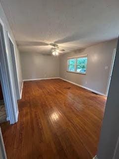 empty room featuring wood finished floors, a ceiling fan, and baseboards