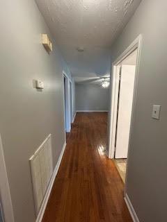 corridor featuring a textured ceiling, wood finished floors, and baseboards