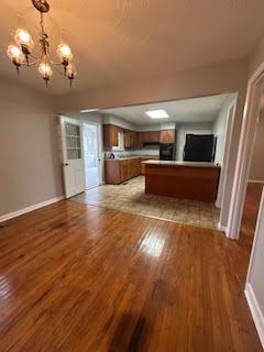 unfurnished living room featuring a chandelier, wood finished floors, and baseboards