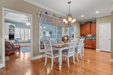 dining area with baseboards, ornamental molding, light wood-style flooring, and a notable chandelier