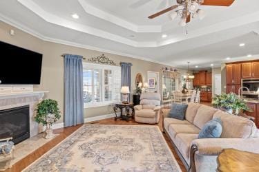 living room featuring recessed lighting, a raised ceiling, a glass covered fireplace, wood finished floors, and baseboards