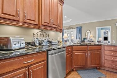 kitchen featuring a toaster, stainless steel dishwasher, brown cabinetry, dark stone countertops, and crown molding