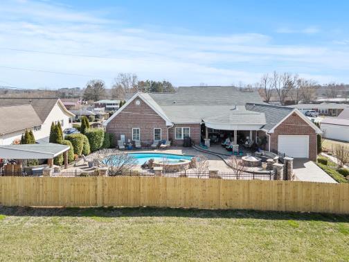 rear view of house featuring a fenced front yard, a fenced in pool, a lawn, and concrete driveway