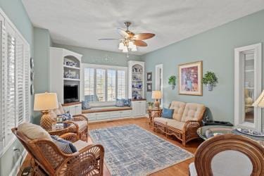 living area with ceiling fan, a fireplace, and wood finished floors